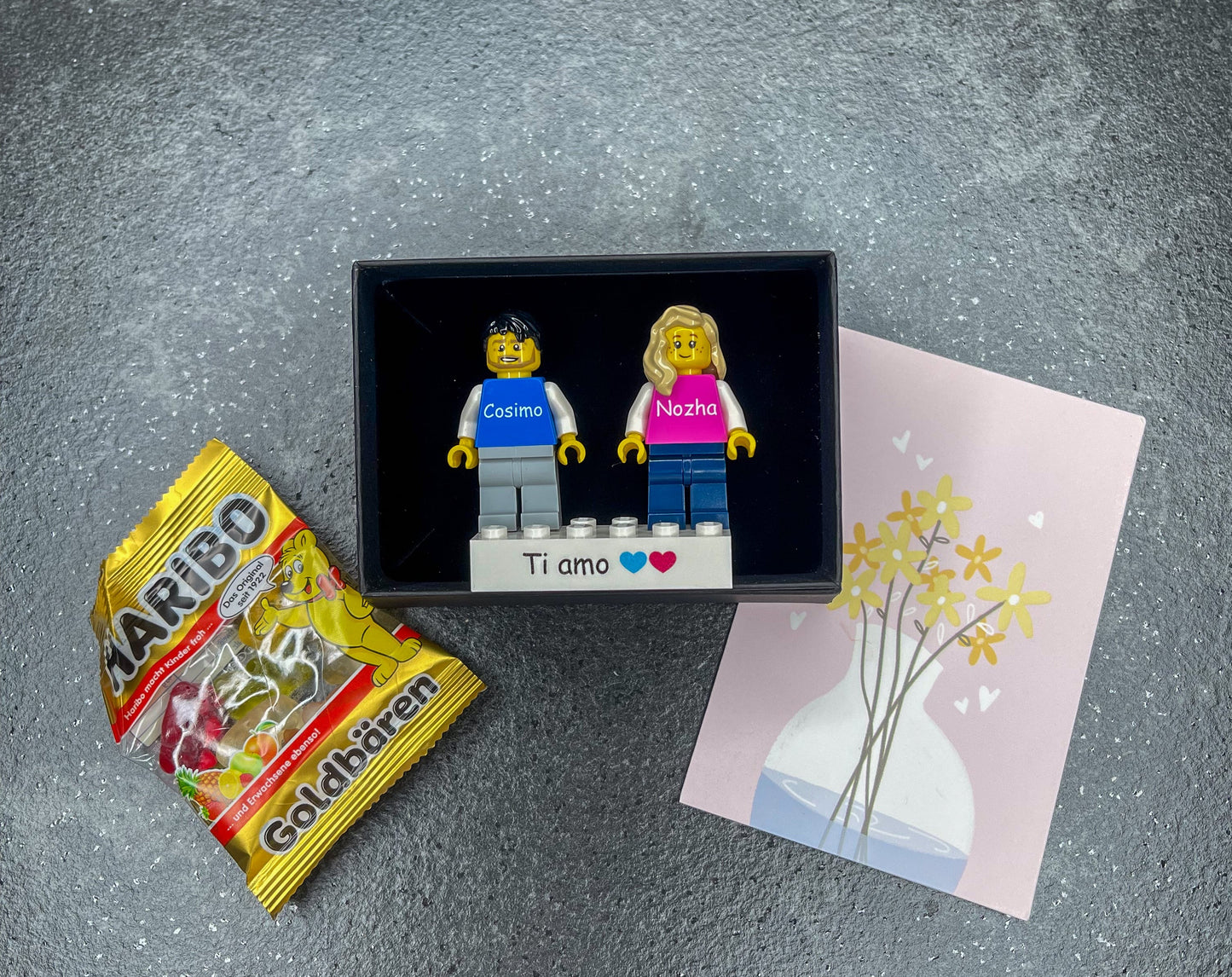 Zwei Personalisierte LEGO® Minifiguren auf einem individuellen Stein mit einer Geschenkbox und Grußkarte